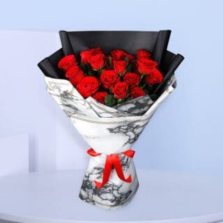 A bouquet of red roses wrapped in white and black marble-patterned paper tied with a red ribbon.