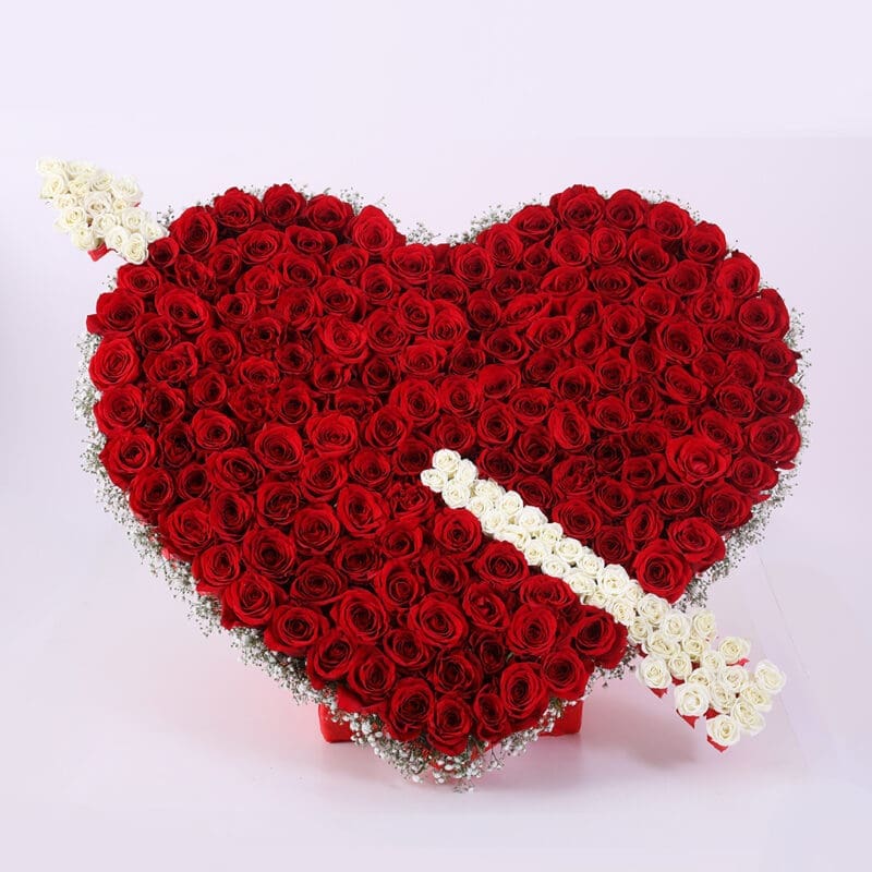 01 A heart-shaped arrangement of red roses with a white arrow made of roses and baby's breath piercing through it.