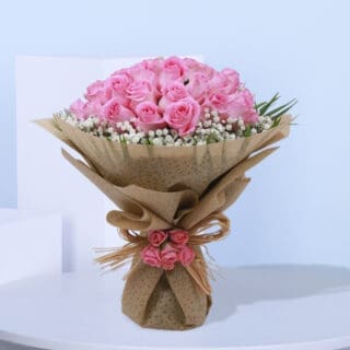 A bouquet of pink roses with baby's breath wrapped in brown paper and tied with a natural coir.