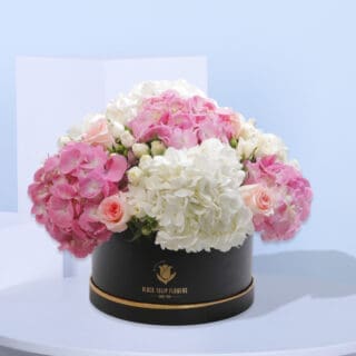 Pink and white hydrangeas and roses in a black hatbox.