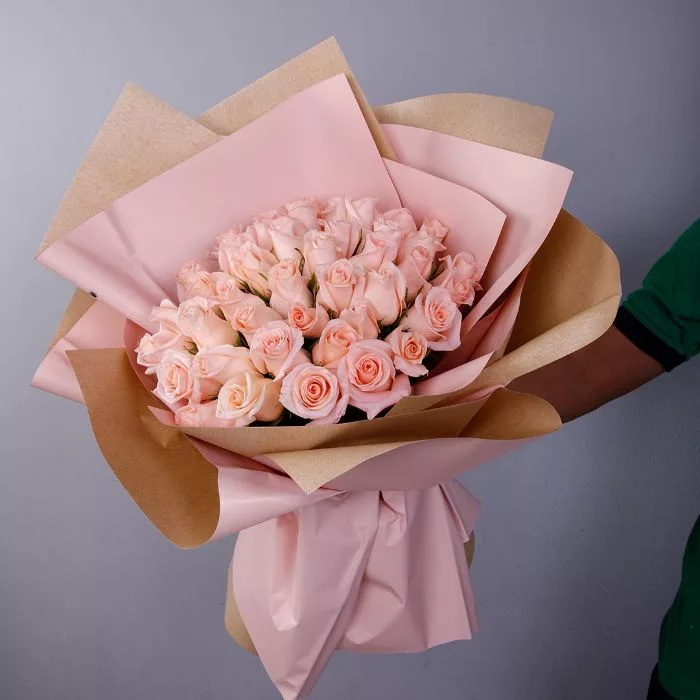 A large bouquet of pink roses wrapped in brown and pink paper.