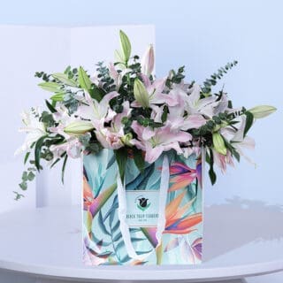 A vibrant bouquet of pink lilies in a colorful floral gift bag. A be