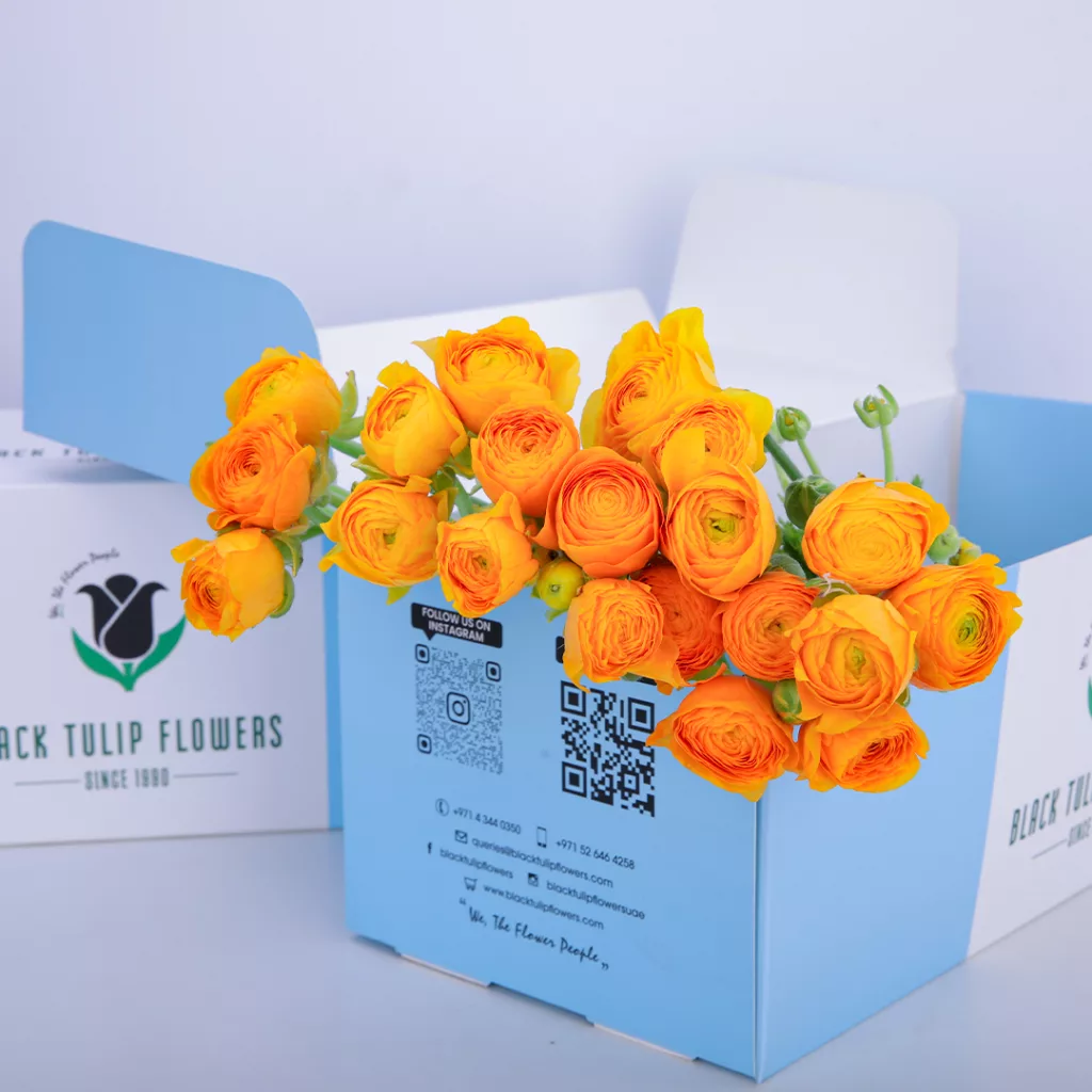 A blue coloured box filled with vibrant yellow Ranunculus flowers, showcasing their delicate petals.