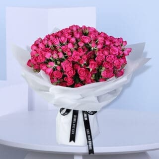 A large bouquet of deep pink spray roses wrapped in white paper with black ribbons.