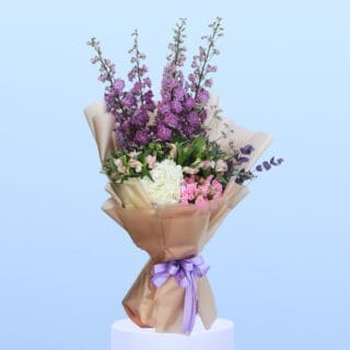 Mixed flowers beautifully arranged in a light brown wrap, elegantly tied with a lavender shade ribbon.