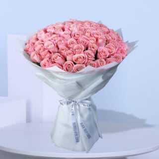 A large bouquet of light pink roses wrapped in white paper with white ribbons.