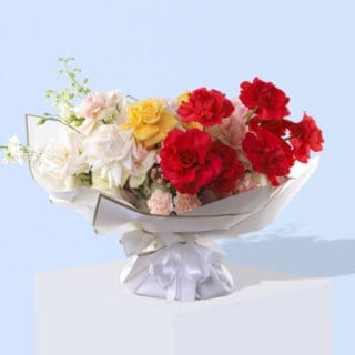 A bouquet featuring mixed roses,carnations, and green foliage, wrapped in white paper with a gold trim and a white ribbon.