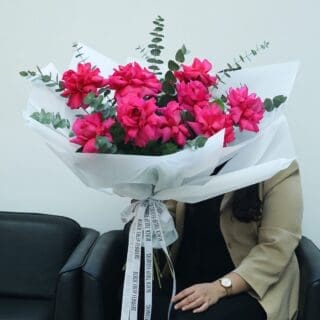 Pink rose bouquet with eucalyptus in white wrap, tied with white ribbon.
