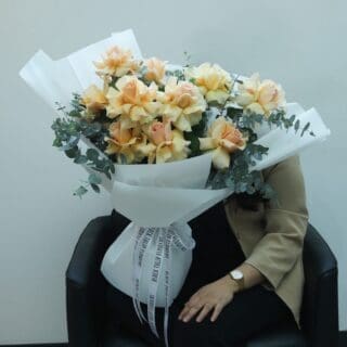 A bouquet of delicate peach roses and fresh eucalyptus, elegantly wrapped in white and tied with a matching white ribbon.