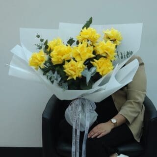 A large bouquet of bright yellow roses wrapped in white paper with green eucalyptus leaves.