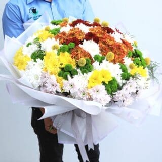 A large bouquet of colourful chrysanthemums with green craspedia, wrapped in white paper with a grey ribbon.