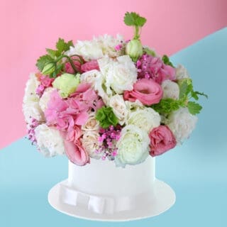 Elegant arrangement of white and pink flowers with lush greenery in a chic white hat box.