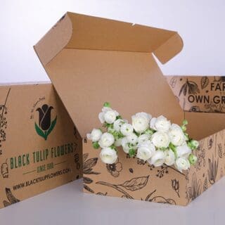A cardboard box filled with a bunch of white Ranunculus flowers, showcasing their delicate petals and vibrant beauty.