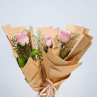 A bouquet of pink roses wrapped in brown paper.