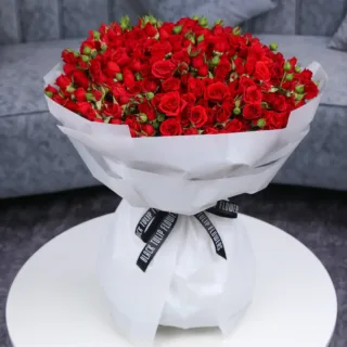 A large bouquet of red spray roses wrapped in white adorned with a black ribbon.