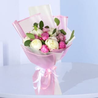 A bouquet of pink and white peonies wrapped in pink tissue paper, tied with a white ribbon