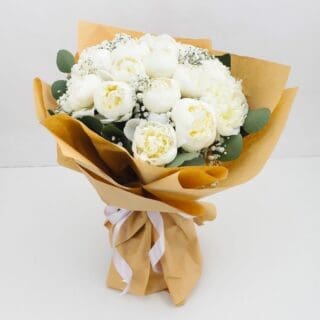 A bouquet of white peonies and baby's breath wrapped in brown paper.