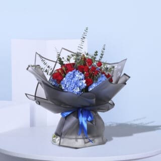 Stunning floral gift of red roses and blue hydrangeas, wrapped in black paper with a blue ribbon