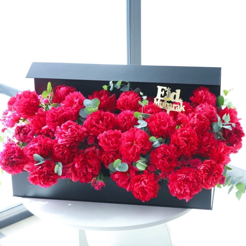 Eid Rejoice Flower Box (1) A black box filled with dark pink peonies and greenery. The lid of the box has "Eid Mubarak" written on it in gold.