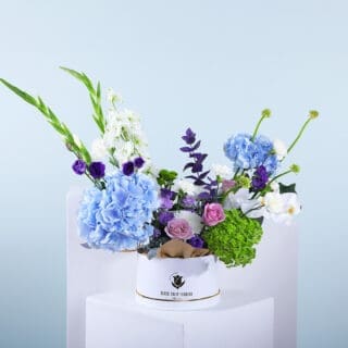 A colourful mixed flower arrangement in a white round box.