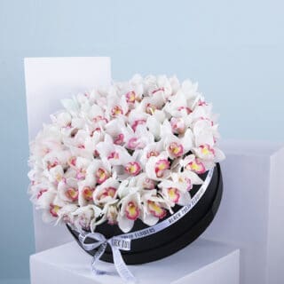 White orchid arrangement in a round black hat box.