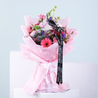 A colorful mixed flower bouquet wrapped in pink tissue paper and tied with a black ribbon featuring the Black Tulip Flowers
