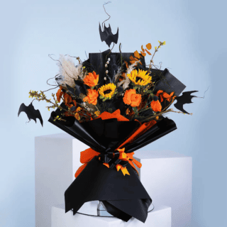 A Halloween bouquet featuring 5 orange roses, 2 sunflowers, forsythia, salix, dry eucalyptus, in a black bouquet with bat-shaped accents.