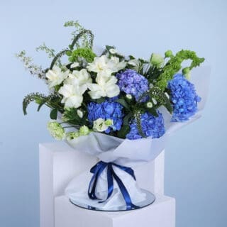 Elegant floral arrangement with blue hydrangeas, white flowers, and greenery.