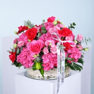 Vibrant pink arrangement of roses, hydrangeas, and other blooms in a woven basket.