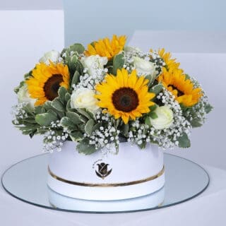 A circular box filled with a bouquet of bright yellow sunflowers and white roses.