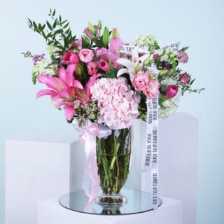 Pink flower arrangement with lilies, tulips, hydrangeas, and other blooms in a glass vase.