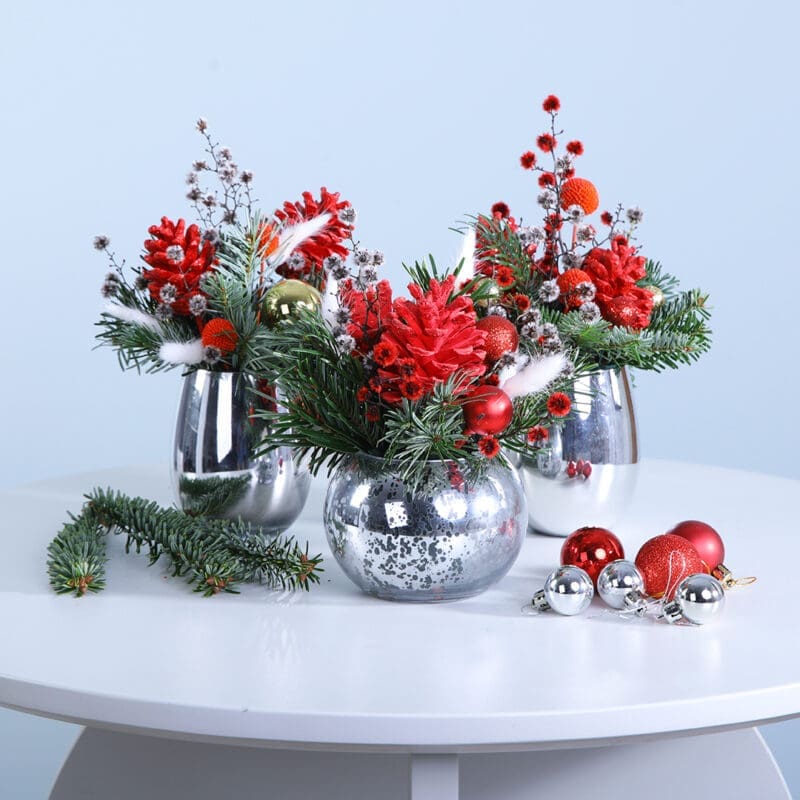 A trio of silver vases filled with vibrant Christmas flowers and decorative elements, enhancing the festive atmosphere.