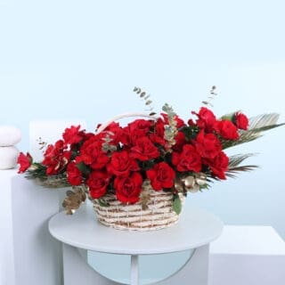 A wicker basket brimming with red roses, spilling over the sides, accented with gold details and fresh eucalyptus leaves.