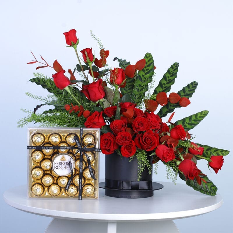 06 25 red roses, vibrant eucalyptus, lush greens, in a black hat box with Ferrero Rocher chocolates.