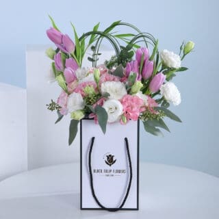 A bouquet of pink and white flowers, including tulips and eustoma, arranged in a white paper bag
