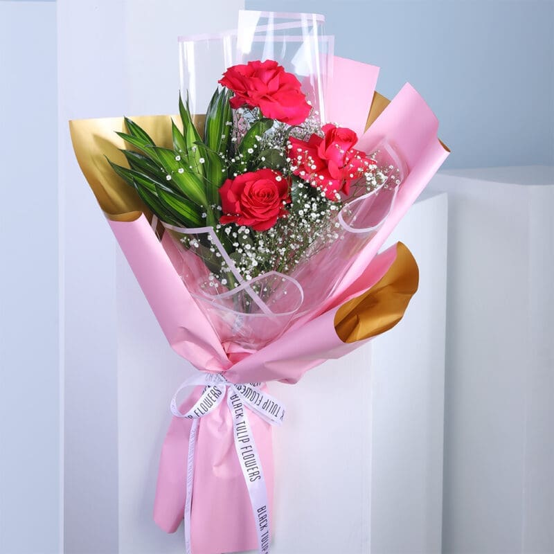 01 A bouquet of red roses wrapped in pink and gold paper with a white ribbon.