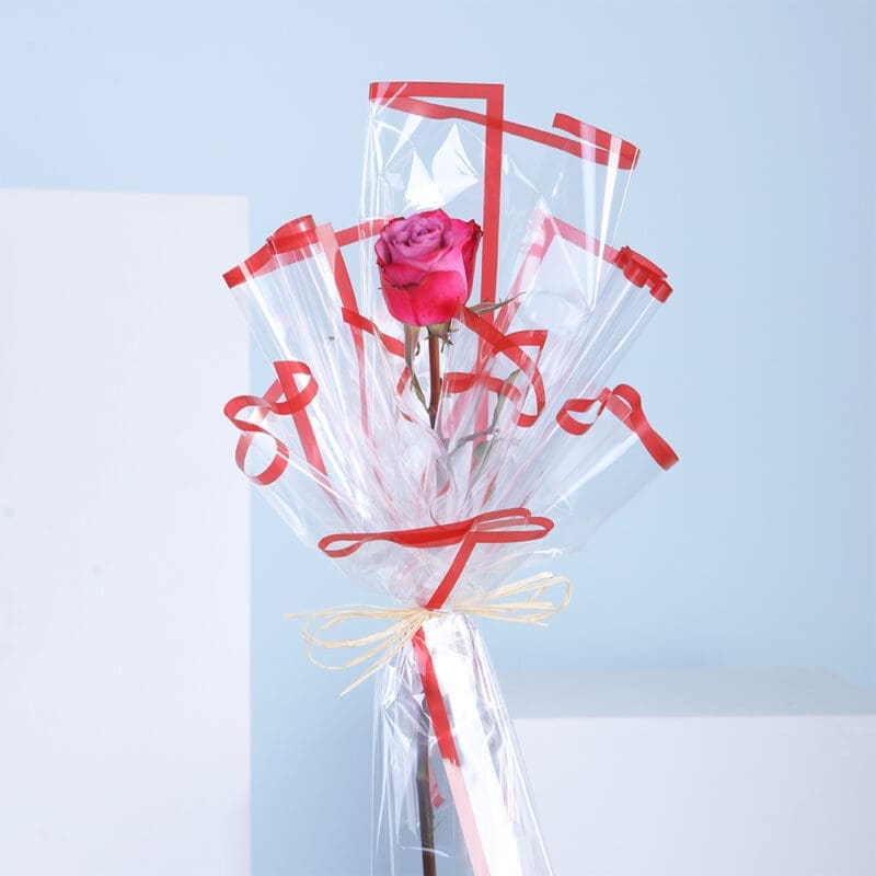 01 A single rose wrapped in cellophane with red ribbons.