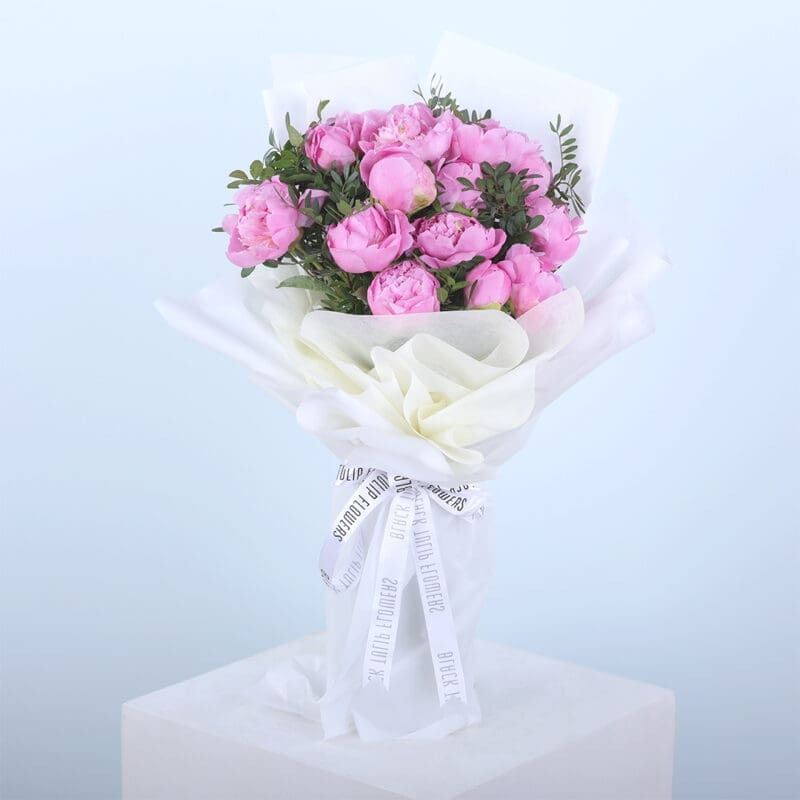 01 A bouquet of pink peonies wrapped in white paper, tied with a ribbon.