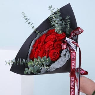 A vibrant mix of Explorer roses paired with fresh eucalyptus, elegantly wrapped in black and tied with white and maroon ribbon