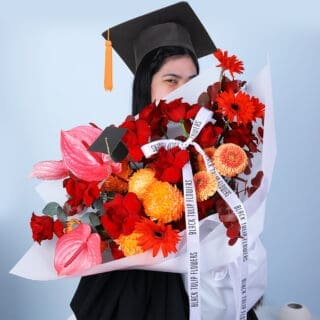 A graduate happily holding a graduation bouquet with red, orange and peach flowers