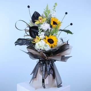 A tall, elegant bouquet featuring yellow sunflowers, white lilies, and black anthuriums, wrapped in black and beige paper.