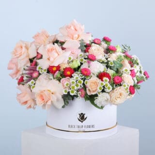 White round box containing peach roses, Santini chrysanthemums, veronica stems, and eucalyptus.