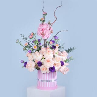 Peach rose, pink hydrangea, purple lisianthus, chrysanthemum, and eucalyptus arranged in a pink box.