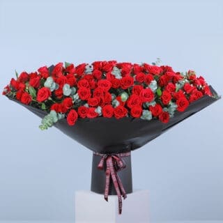Funnel Shape Red Rose bouquet with eucalyptus leaves wrapped in black and tied with pink ribbon