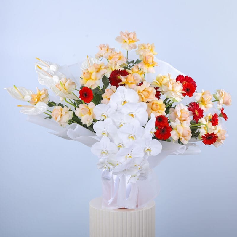 A beautiful arrangement of peach roses, white anthurium, phalaenopsis stems, gerberas, and greens in white wrap