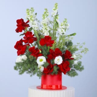Bouquet of red roses, mathiolla, white lisianthus, and greenery arranged in a red hat box