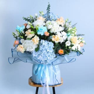  colorful bouquet of blue and white hydrangeas with peach roses, blue roses, and chrysanthemums on a wooden stool