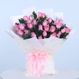 Bouquet of 30 pink roses wrapped in white with fresh green leaves.