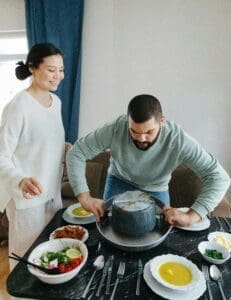 A couple standing together in a kitchen, plating food onto plates. They are smiling and seem to be enjoying the process of preparing a meal together.