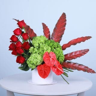 A luxurious Valentine's Day flower box overflowing with red roses, exotic anthuriums, and lush green hydrangea.
